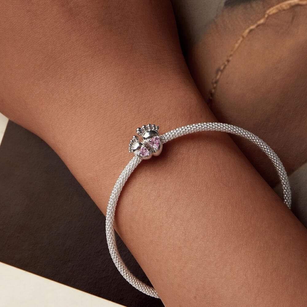 Sterling silver baby feet charm with two pink heart crystals and polished newborn footprint details.