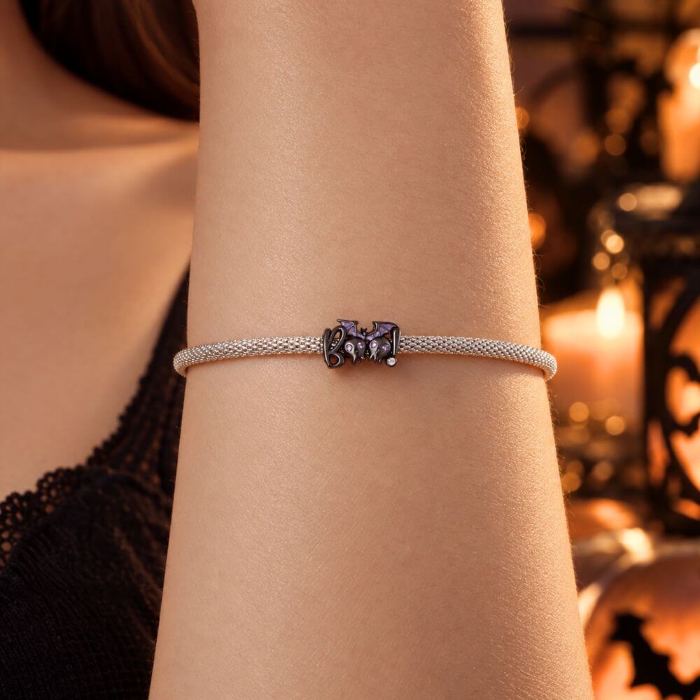 Black skull and bat charm with purple crystal eyes, glitter wings, and playful spooky Halloween details.