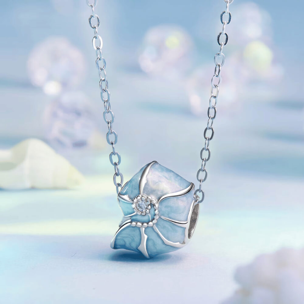 Sterling silver bead charm with blue enamel shell design and central clear gemstone.