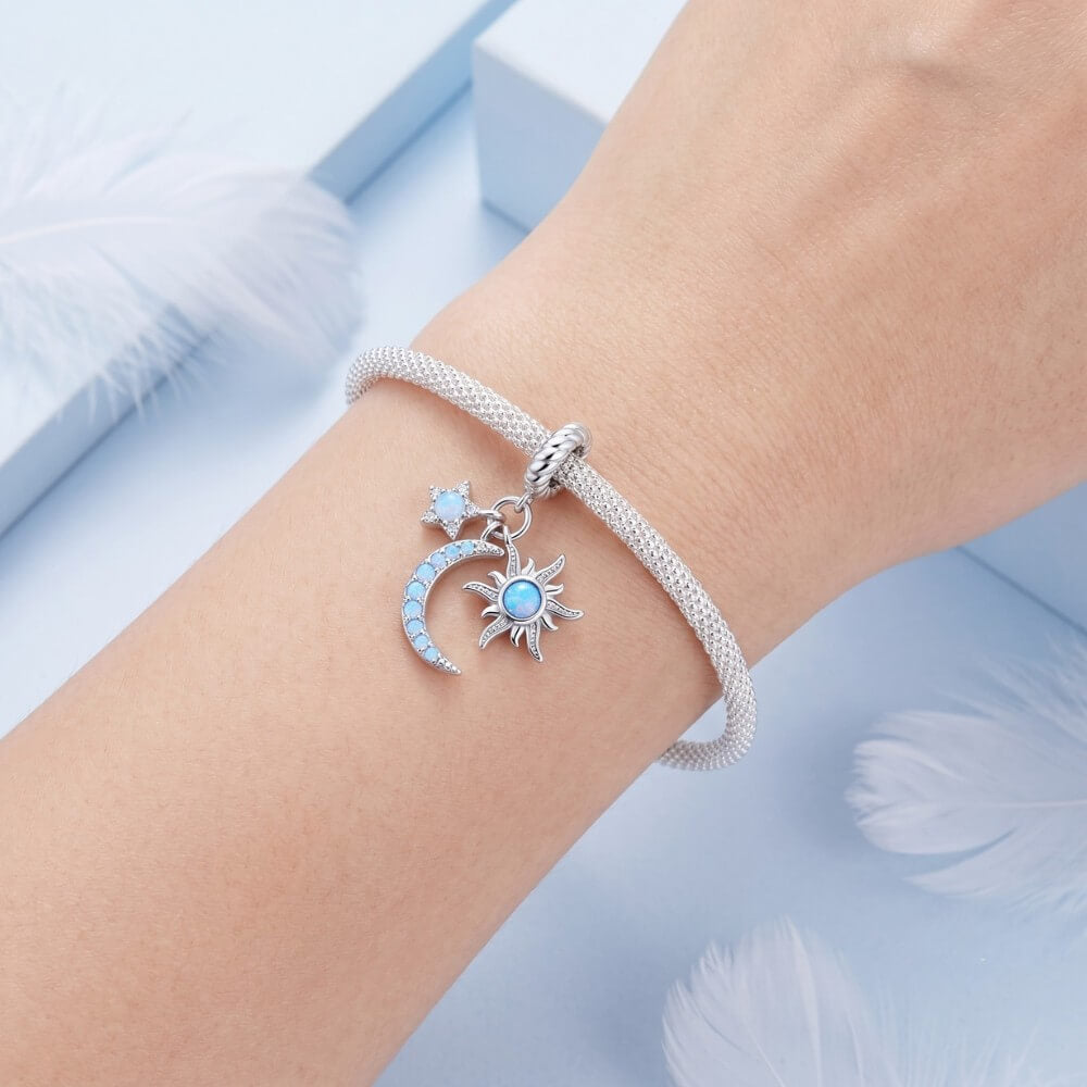 Silver bracelet with moon and sun charms on a wrist against a light blue background
