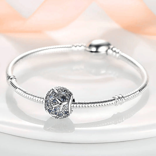 Sterling silver charm covered in light and dark blue stones with raised airplane motifs across the surface