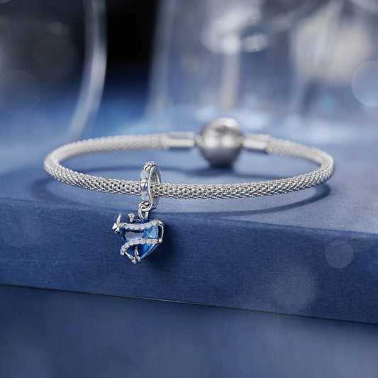 Sterling silver charm with a bright blue faceted heart crystal wrapped in silver vine-like details and small round light-blue stones on the bail