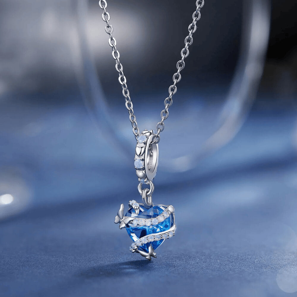 Sterling silver charm with a bright blue faceted heart crystal wrapped in silver vine-like details and small round light-blue stones on the bail