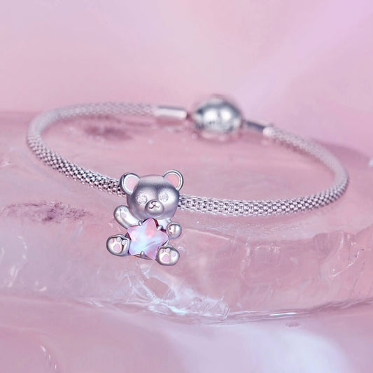 Sterling silver teddy bear charm holding pink star crystal with enamel details.