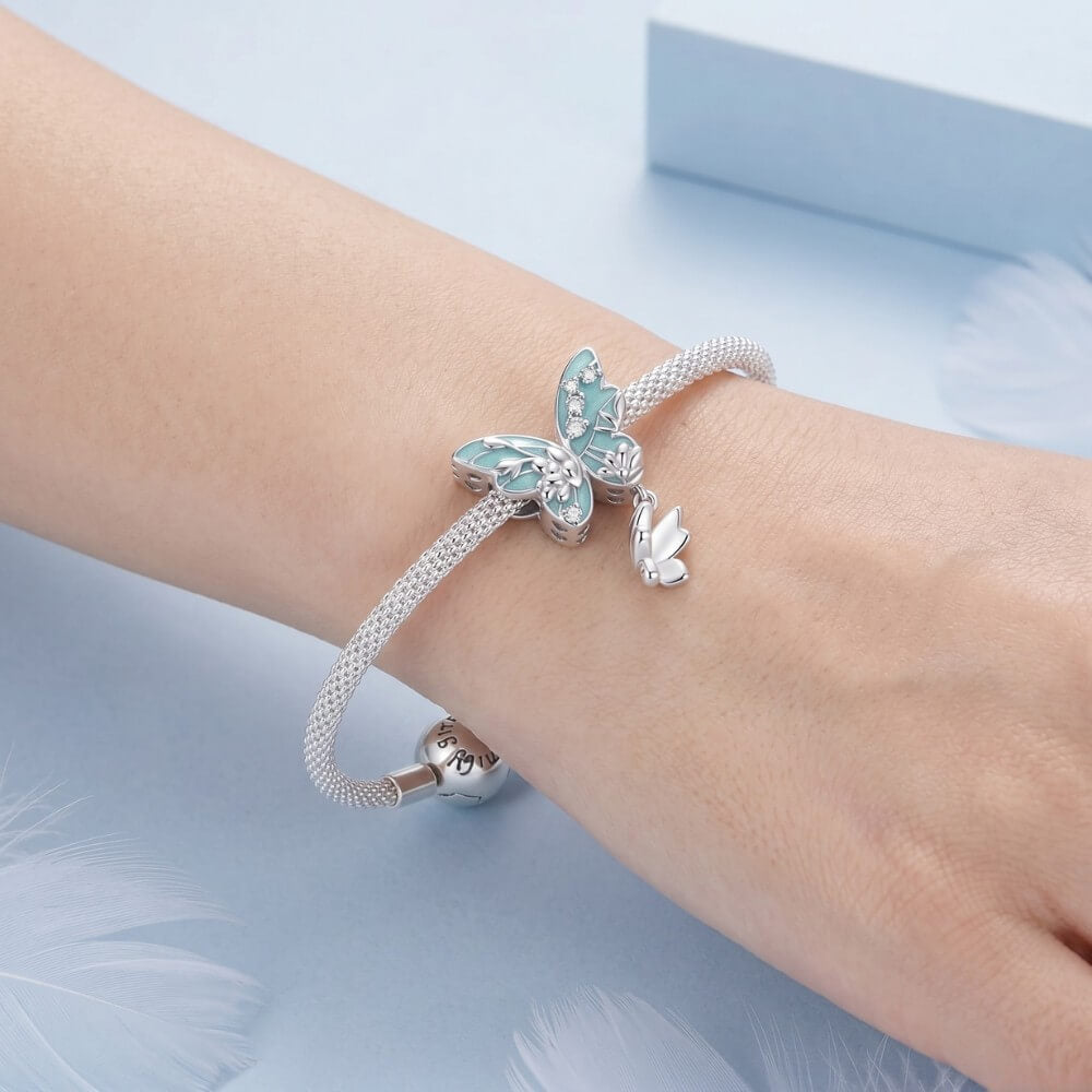 Silver bracelet with butterfly charm on a wrist against a light blue background