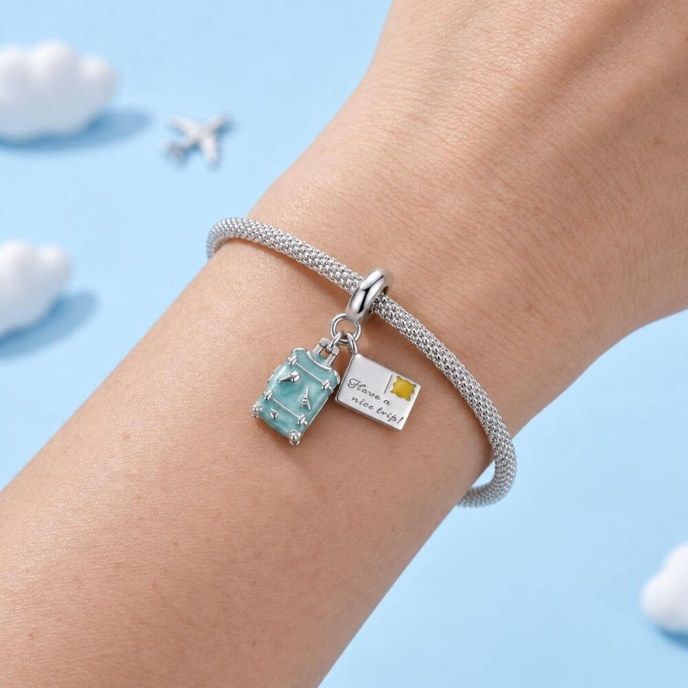 Sterling silver travel charm with turquoise suitcase, postcard, Eiffel Tower, and airplane-inspired details.