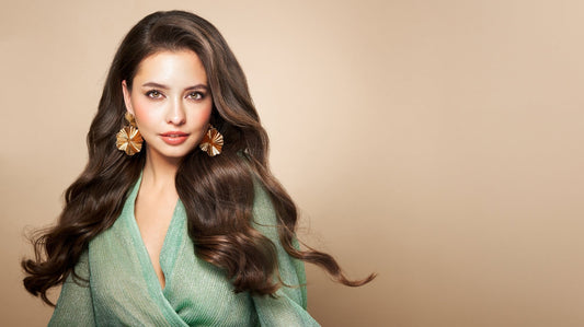Woman wearing gold statement earrings and a green dress against a soft neutral background