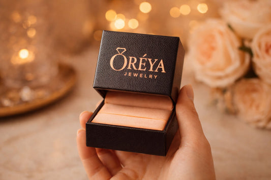 Hand holding an open ORÉYA jewelry gift box with logo on the lid