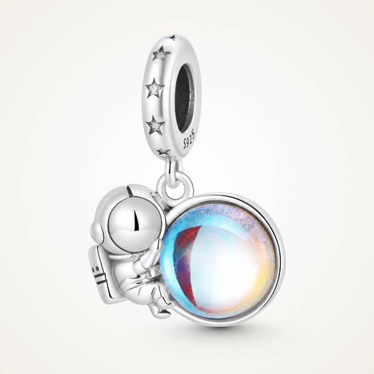 Sterling silver astronaut charm holding an iridescent planet with star details and cosmic blue reflections - ORÉYA