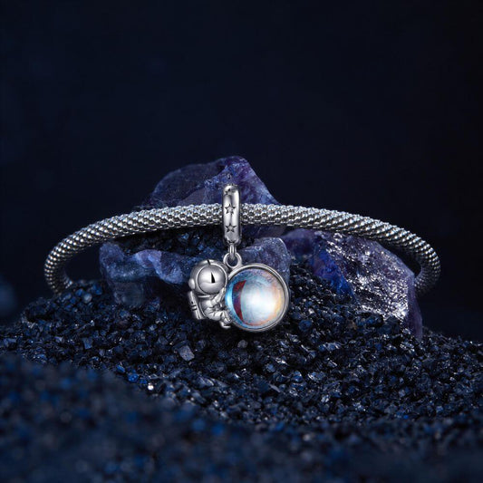 Sterling silver astronaut charm holding an iridescent planet with star details and cosmic blue reflections.