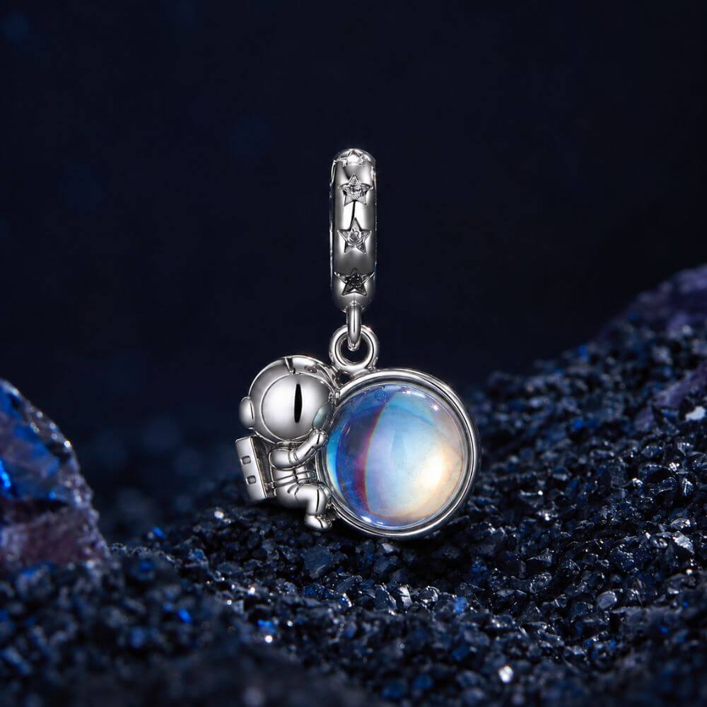 Sterling silver astronaut charm holding an iridescent planet with star details and cosmic blue reflections.