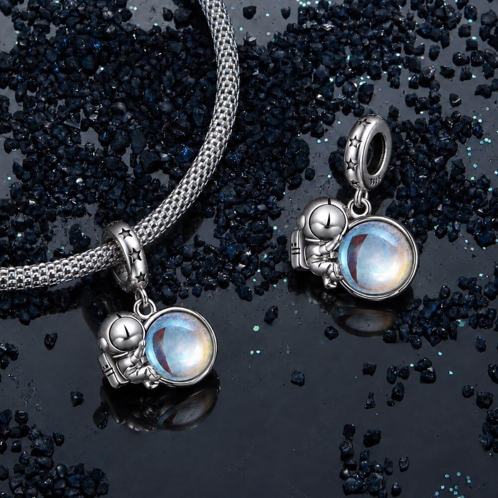 Sterling silver astronaut charm holding an iridescent planet with star details and cosmic blue reflections.