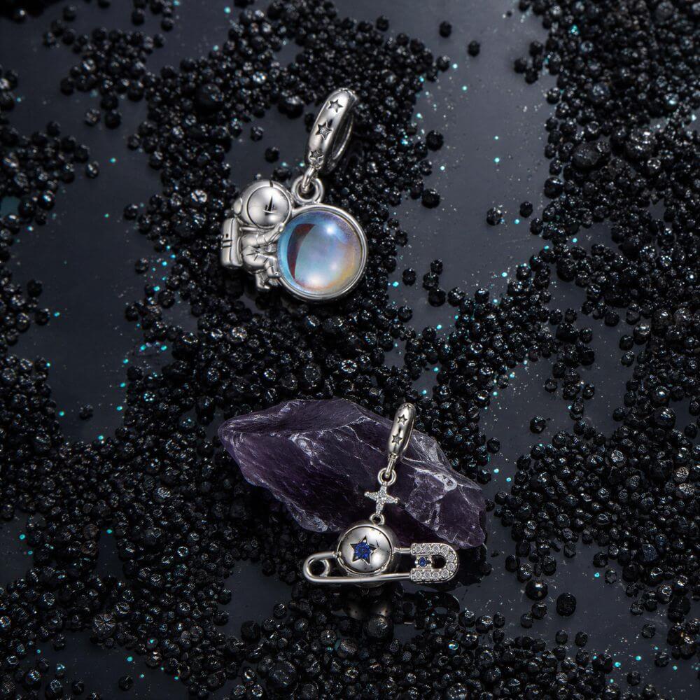 Sterling silver astronaut charm holding an iridescent planet with star details and cosmic blue reflections.