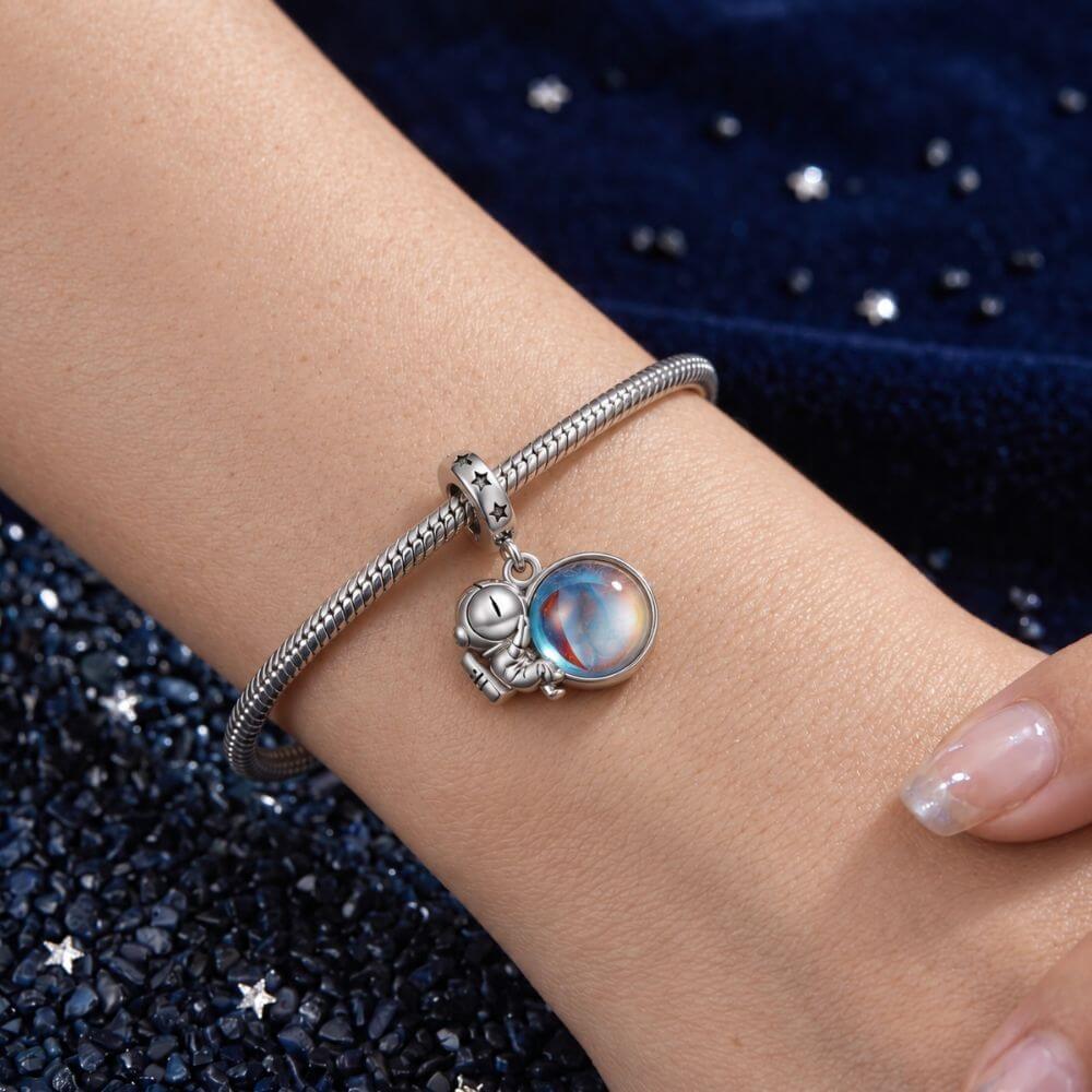 Sterling silver astronaut charm holding an iridescent planet with star details and cosmic blue reflections.