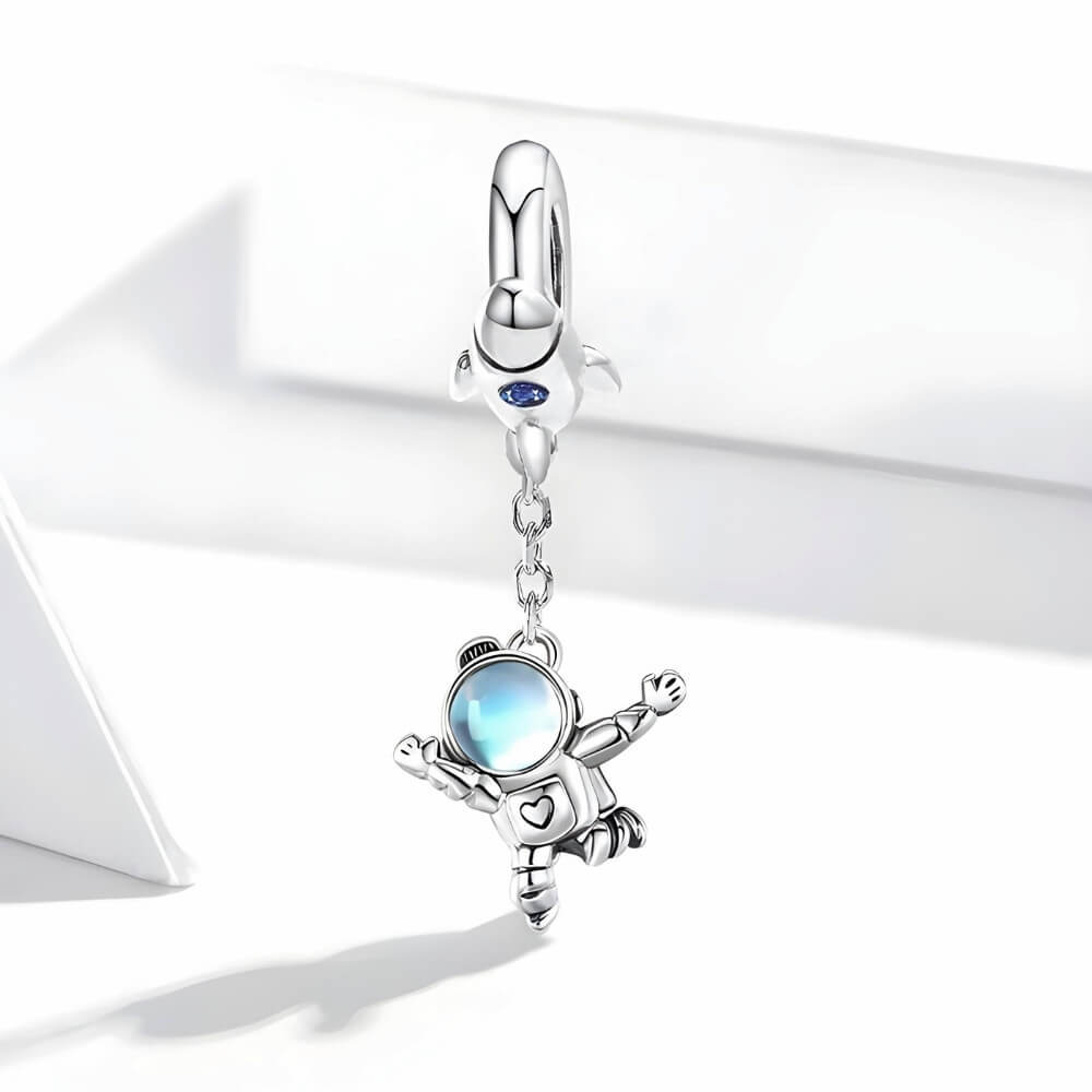Sterling silver astronaut charm hanging from rocket bail with blue glass visor.