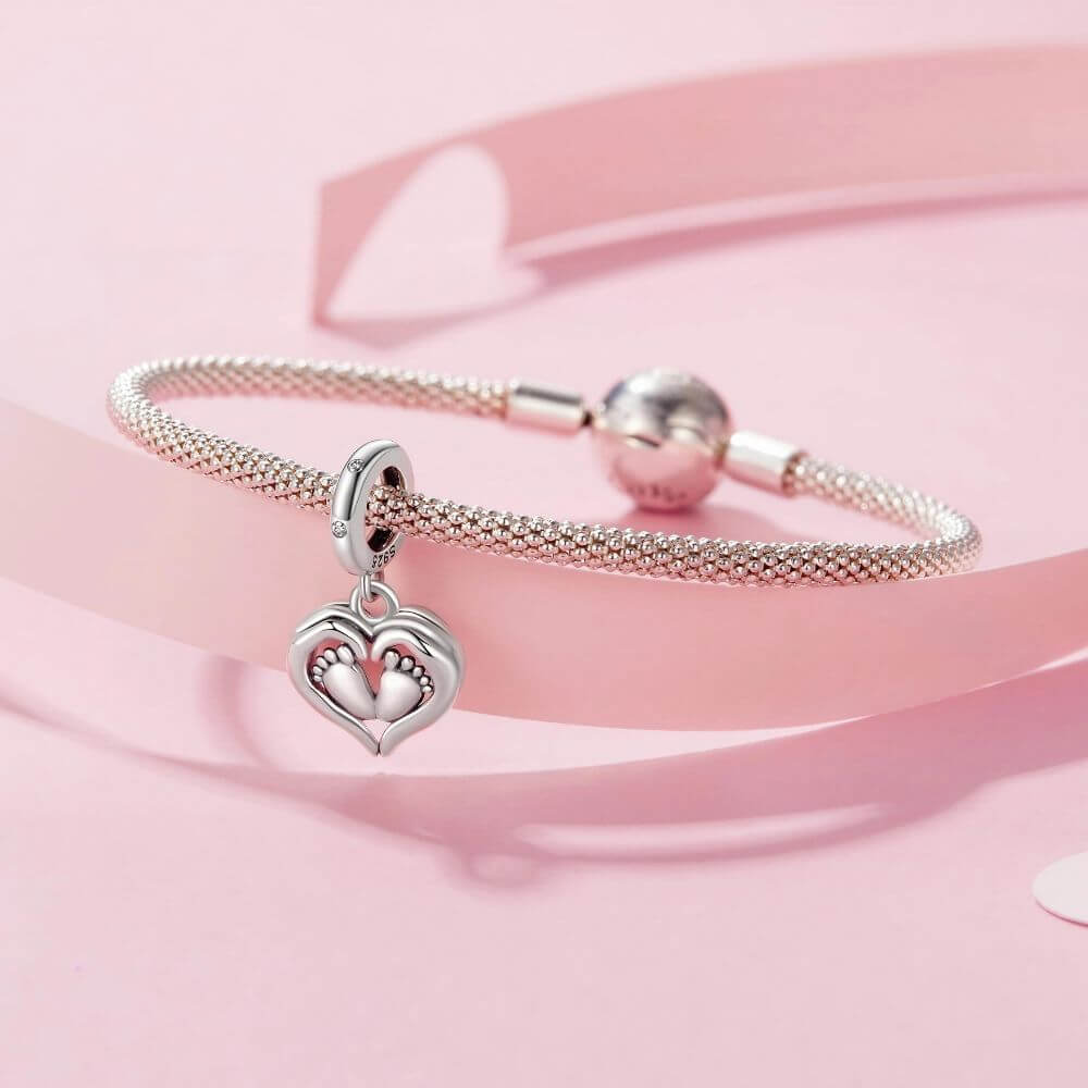 Sterling silver baby feet charm framed by a heart with sparkling crystal accents and delicate polished details.