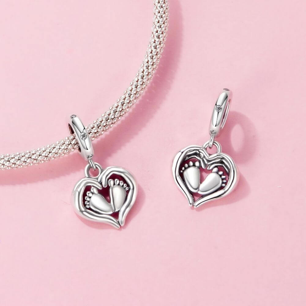 Sterling silver baby feet charm framed by a heart with sparkling crystal accents and delicate polished details.