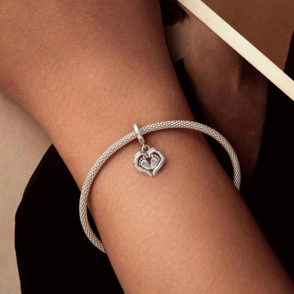 Sterling silver baby feet charm framed by a heart with sparkling crystal accents and delicate polished details.