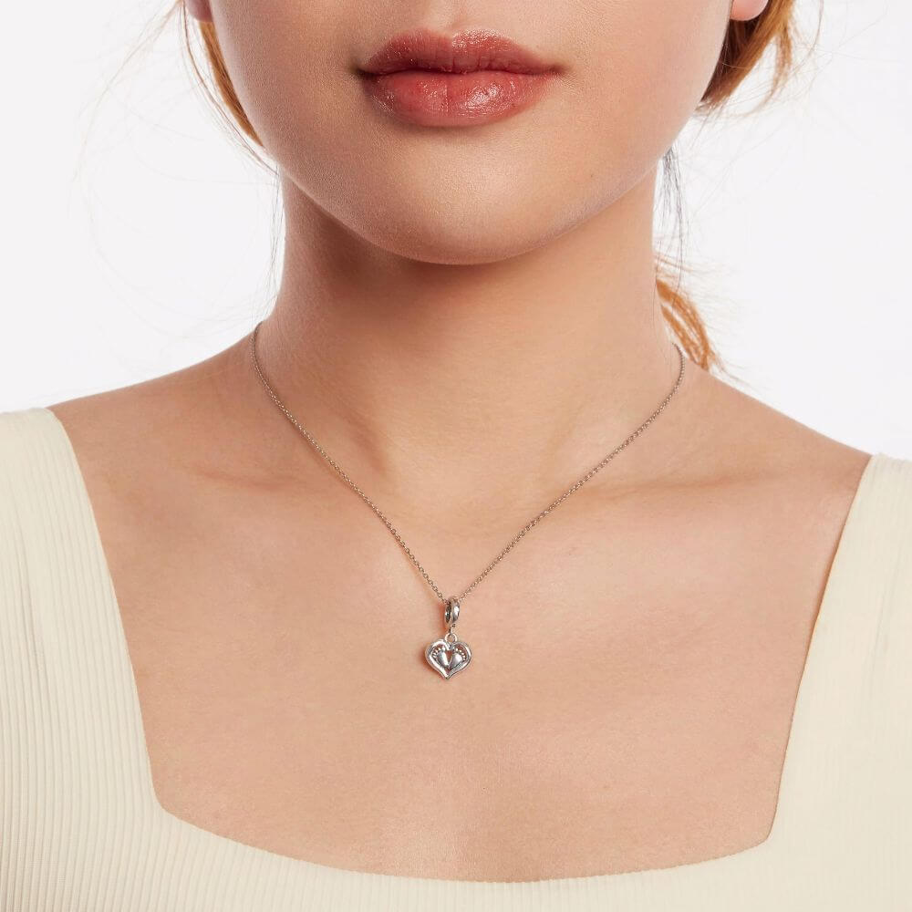 Sterling silver baby feet charm framed by a heart with sparkling crystal accents and delicate polished details.