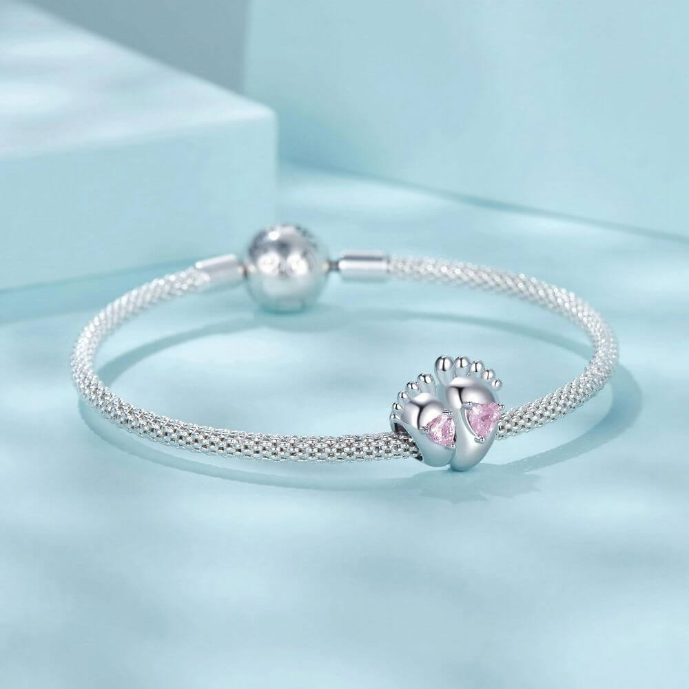 Sterling silver baby feet charm with two pink heart crystals and polished newborn footprint details.