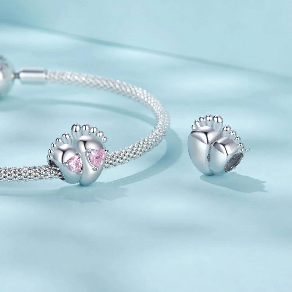 Sterling silver baby feet charm with two pink heart crystals and polished newborn footprint details.