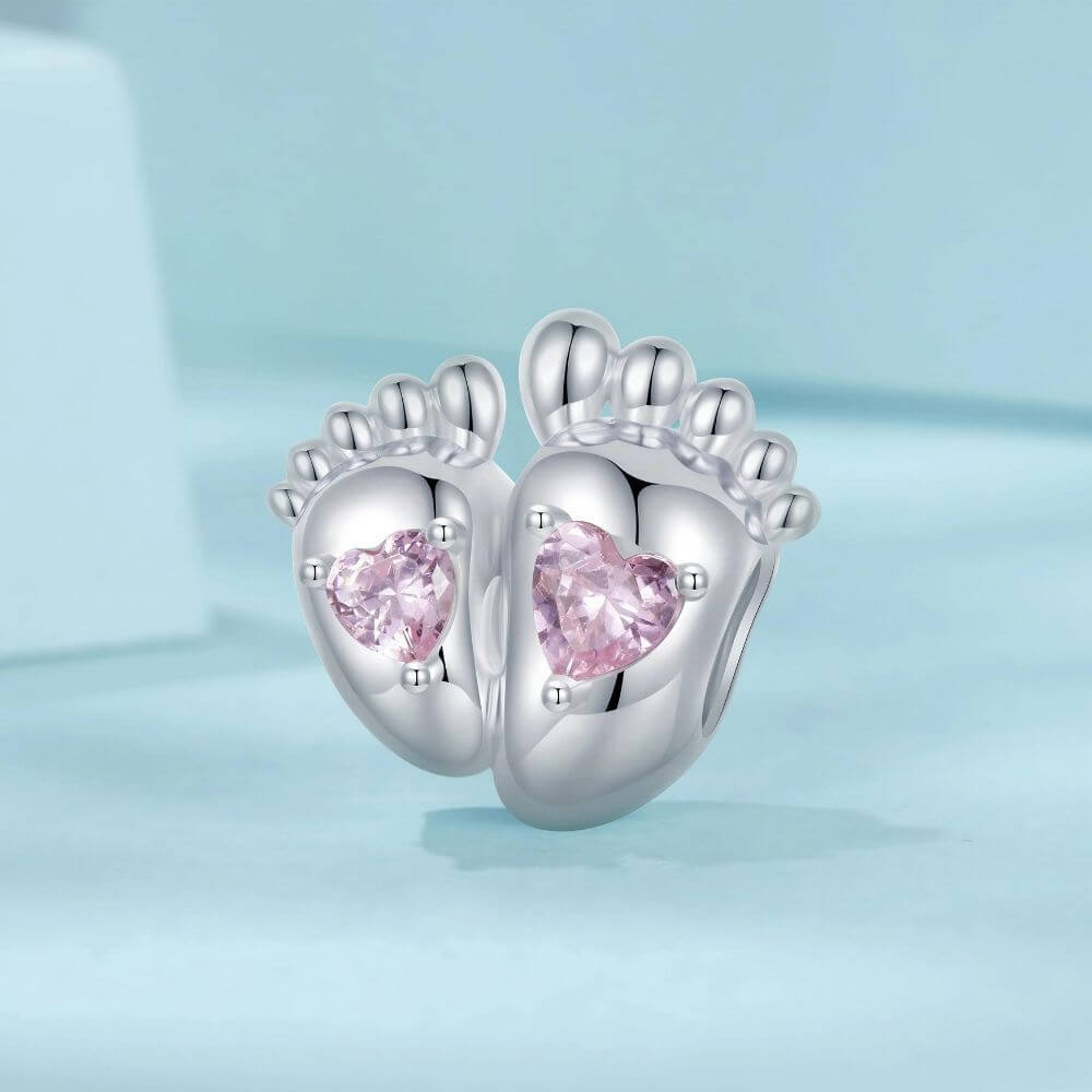 Sterling silver baby feet charm with two pink heart crystals and polished newborn footprint details.