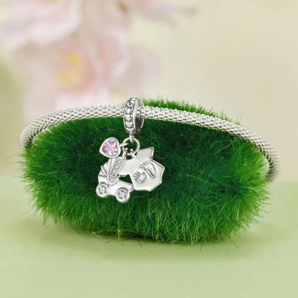 Sterling silver baby charm with stroller, pink heart crystal, house tag, and tiny hand and footprint details.