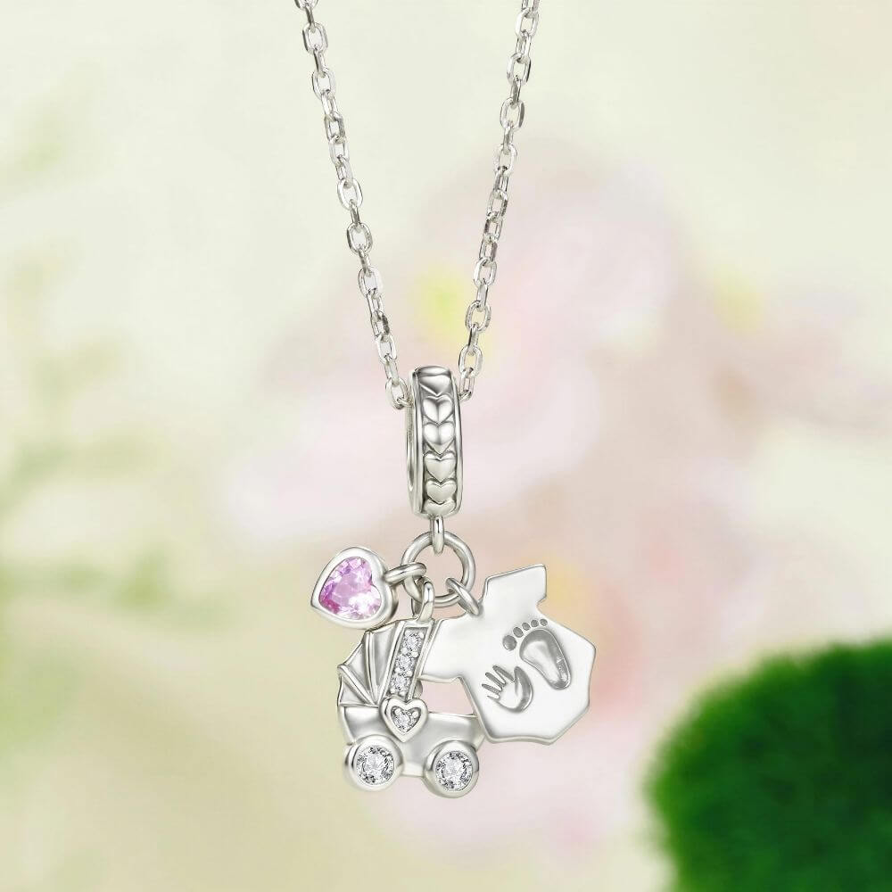 Sterling silver baby charm with stroller, pink heart crystal, house tag, and tiny hand and footprint details.
