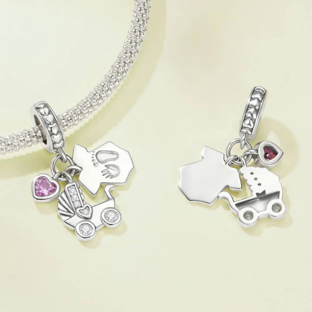 Sterling silver baby charm with stroller, pink heart crystal, house tag, and tiny hand and footprint details.