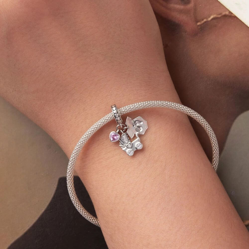 Sterling silver baby charm with stroller, pink heart crystal, house tag, and tiny hand and footprint details.