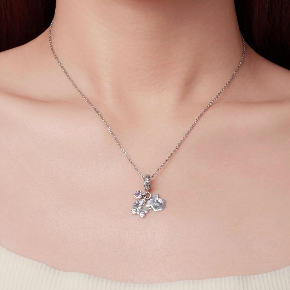 Sterling silver baby charm with stroller, pink heart crystal, house tag, and tiny hand and footprint details.
