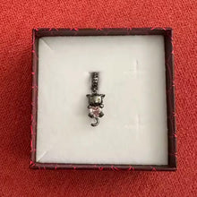 Black-plated silver cat charm holding pink heart-shaped gemstone with green eyes.