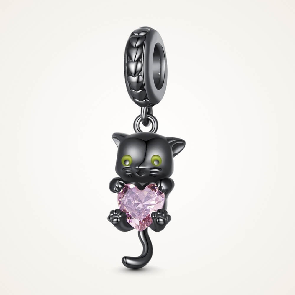 Black-plated silver cat charm holding pink heart-shaped gemstone with green eyes - ORÉYA