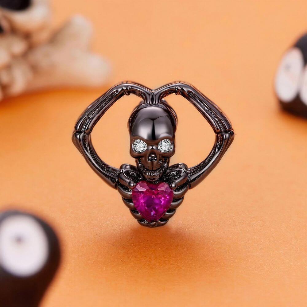 Black skeleton heart charm with crystal eyes, vivid pink heart stone, and gothic skeletal arm details.
