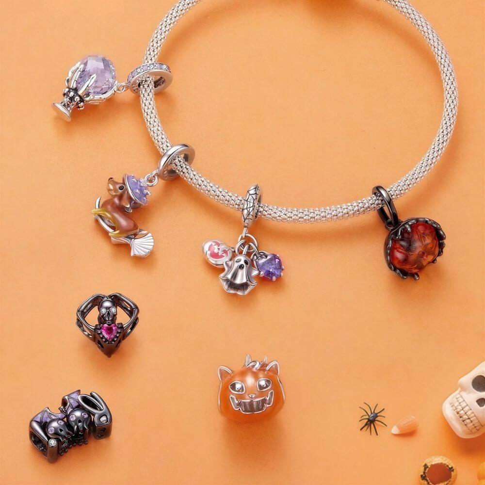 A silver-toned beaded bracelet with multiple Halloween-themed charms, displayed on an orange background with additional matching charms scattered nearby.