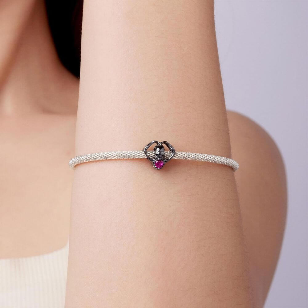 Black skeleton heart charm with crystal eyes, vivid pink heart stone, and gothic skeletal arm details.