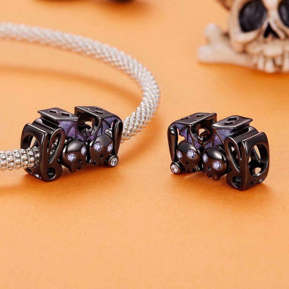 Black skull and bat charm with purple crystal eyes, glitter wings, and playful spooky Halloween details.