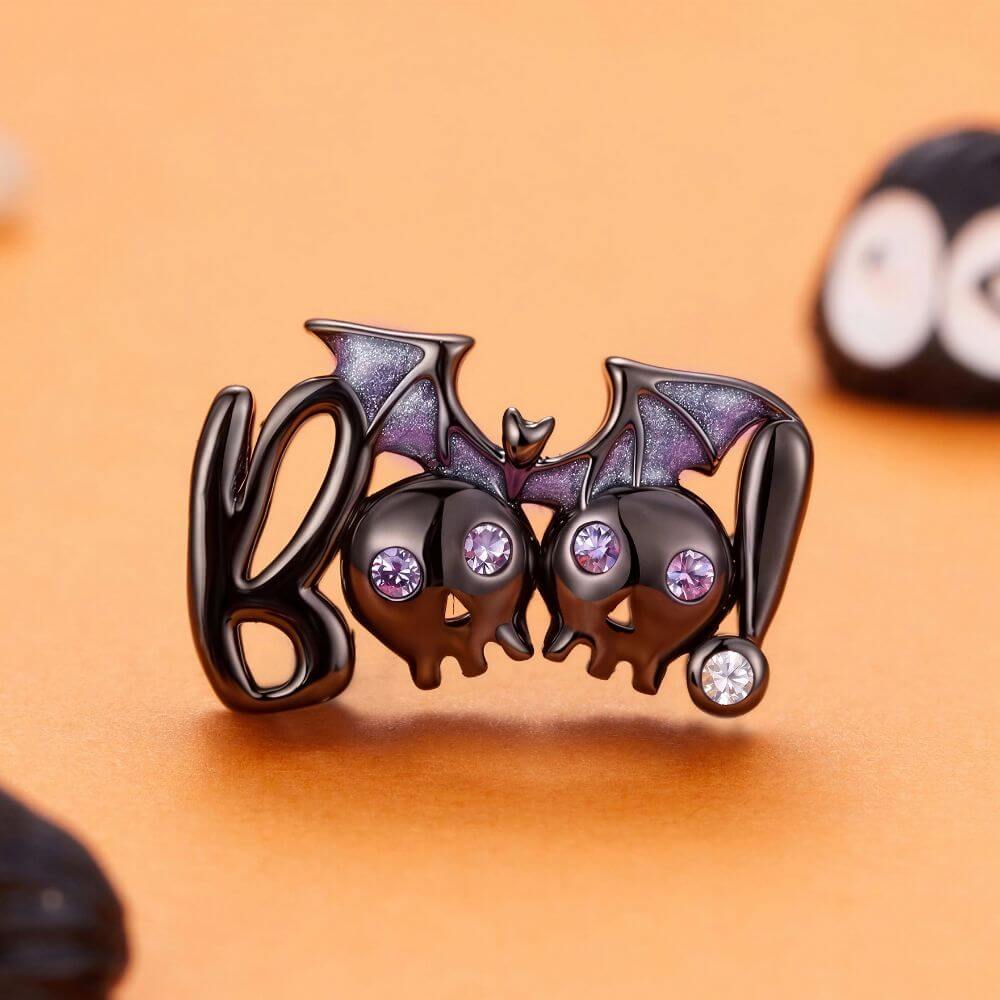 Black skull and bat charm with purple crystal eyes, glitter wings, and playful spooky Halloween details.