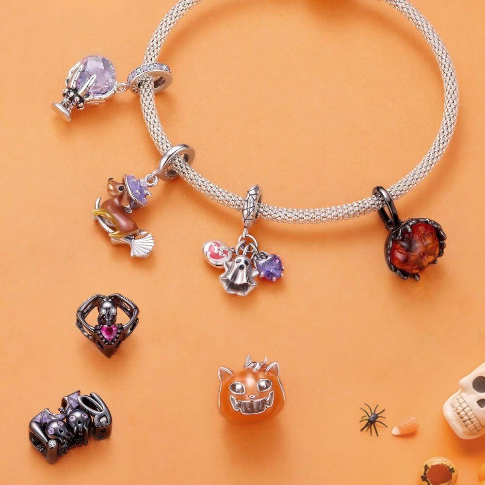 A silver-toned beaded bracelet with multiple Halloween-themed charms, displayed on an orange background with additional matching charms scattered nearby.
