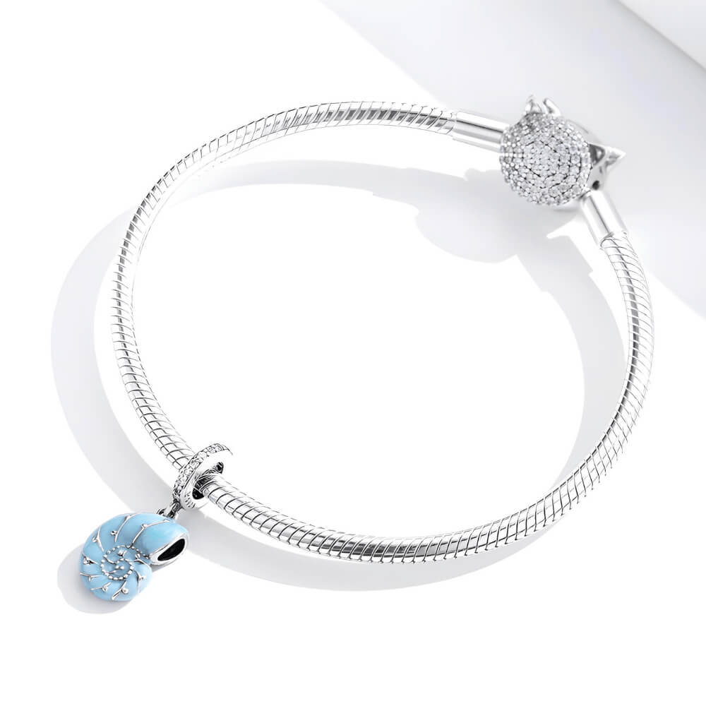 Sterling silver nautilus shell charm with blue enamel and clear gemstones.