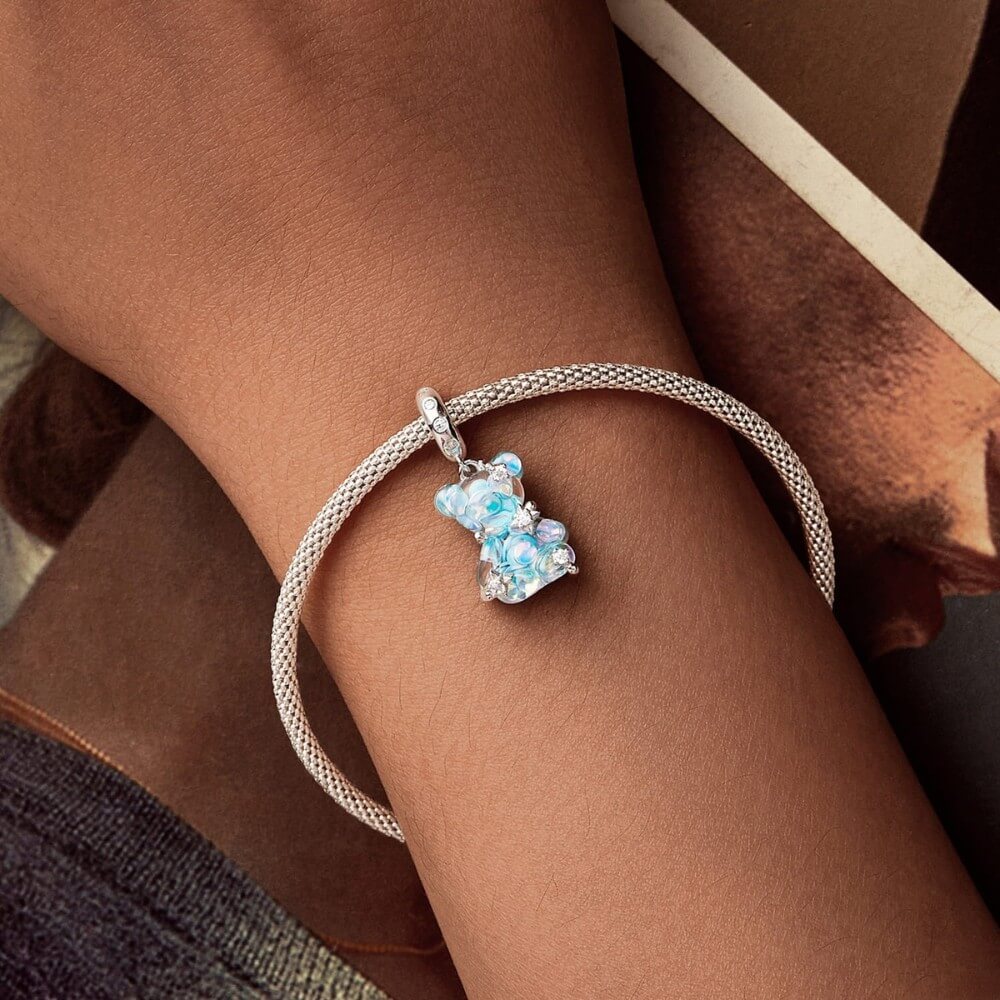 Silver bracelet with a bear-shaped charm on a wrist against a brown background