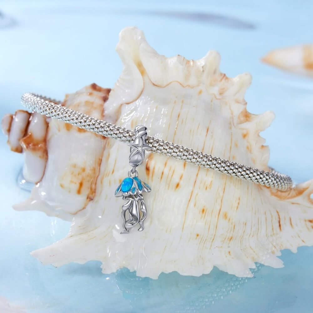 Sterling silver jellyfish charm with blue enamel and flowing ocean details.