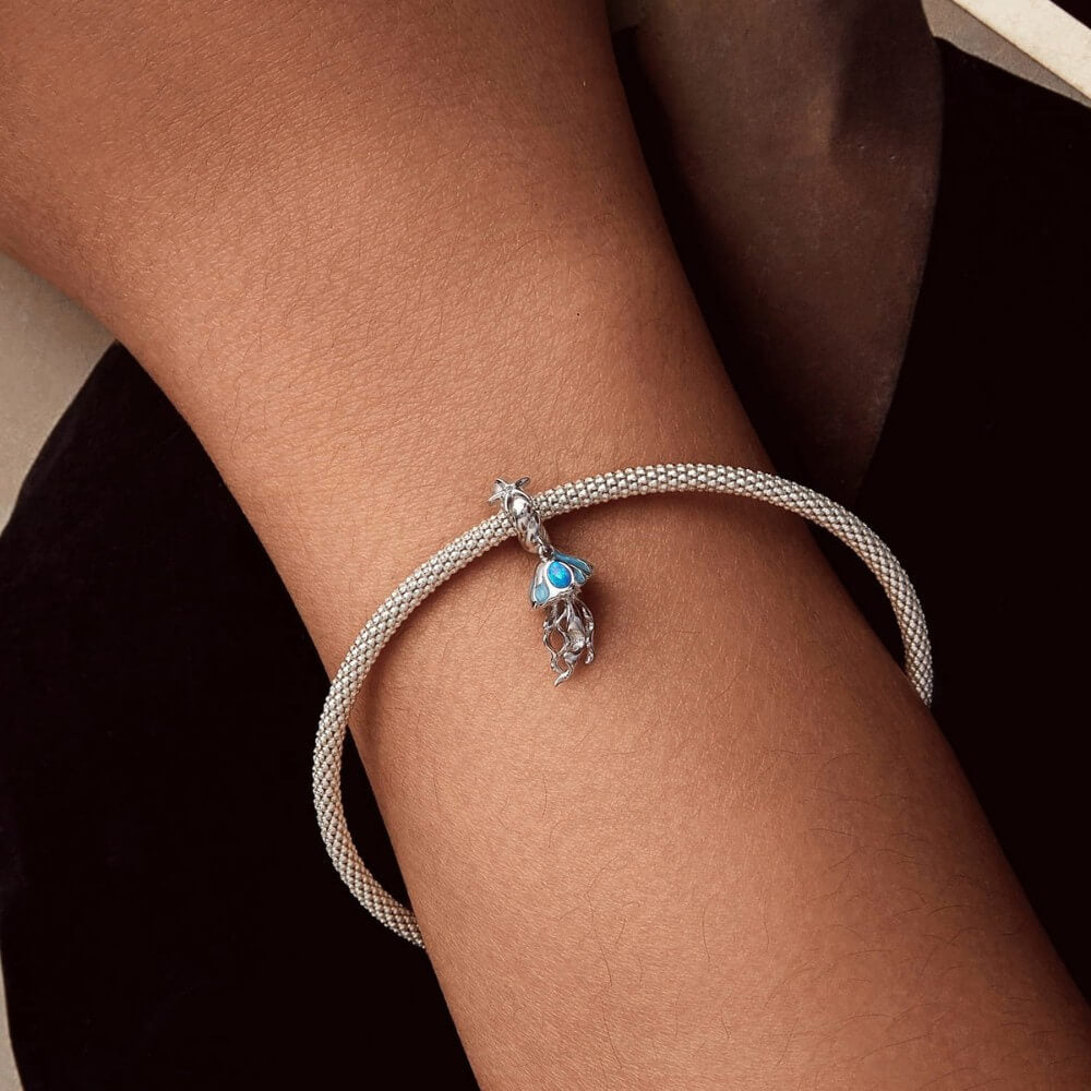 Sterling silver jellyfish charm with blue enamel and flowing ocean details.