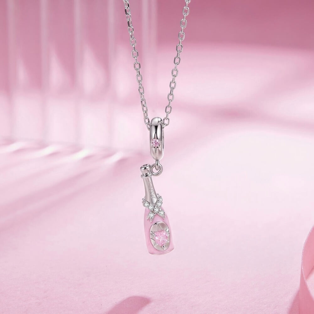 Sterling silver champagne bottle charm with pink enamel, bow detail and heart crystal.