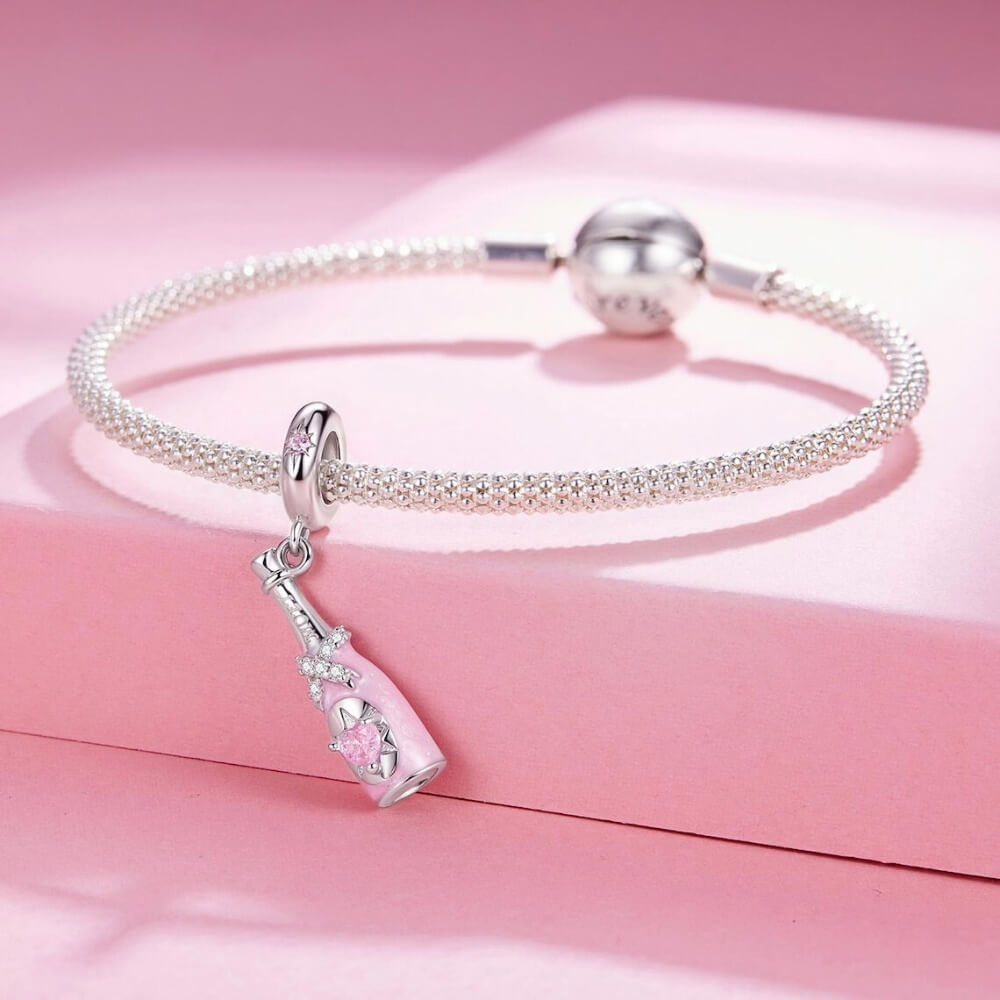 Sterling silver champagne bottle charm with pink enamel, bow detail and heart crystal.