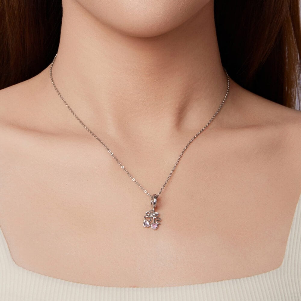 Sterling silver cherry charm with pink heart gemstones and bow detail.