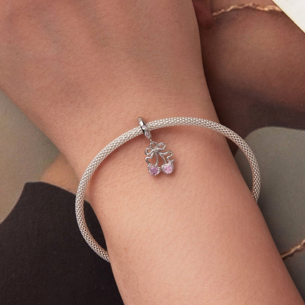 Sterling silver cherry charm with pink heart gemstones and bow detail.