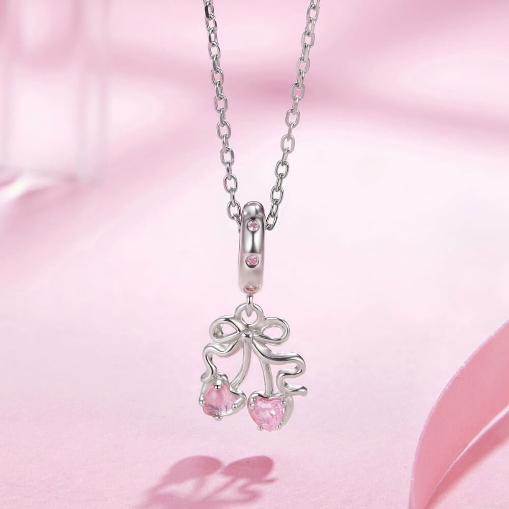 Sterling silver cherry charm with pink heart gemstones and bow detail.