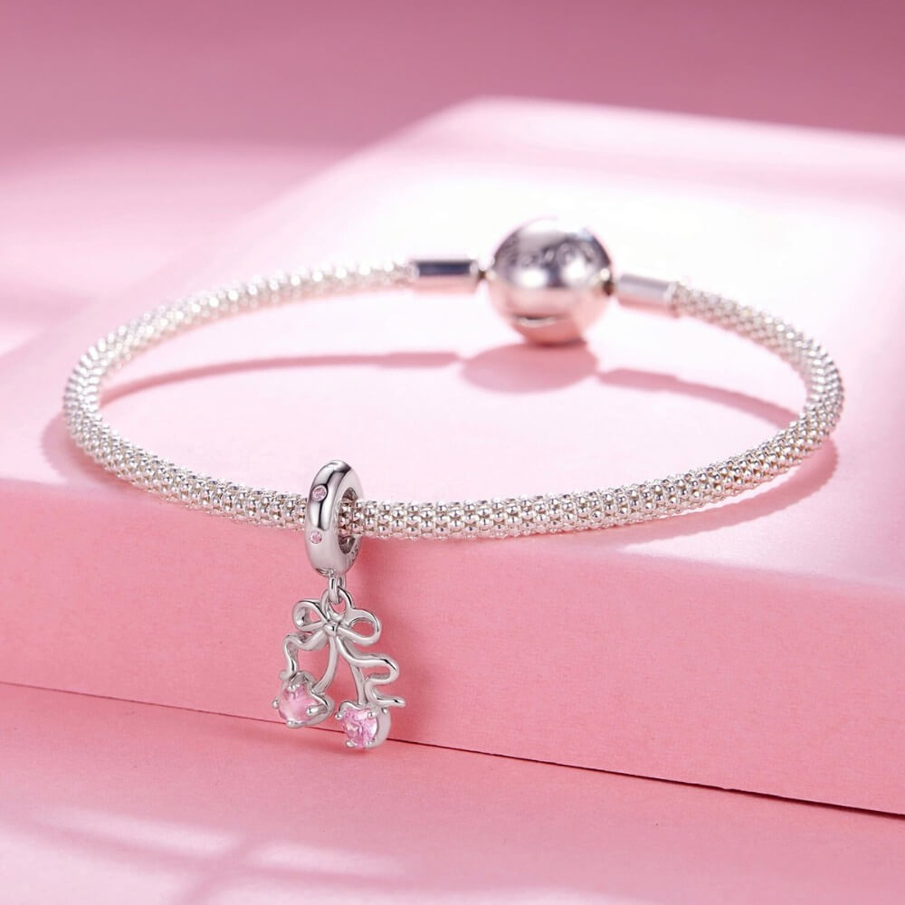 Sterling silver cherry charm with pink heart gemstones and bow detail.