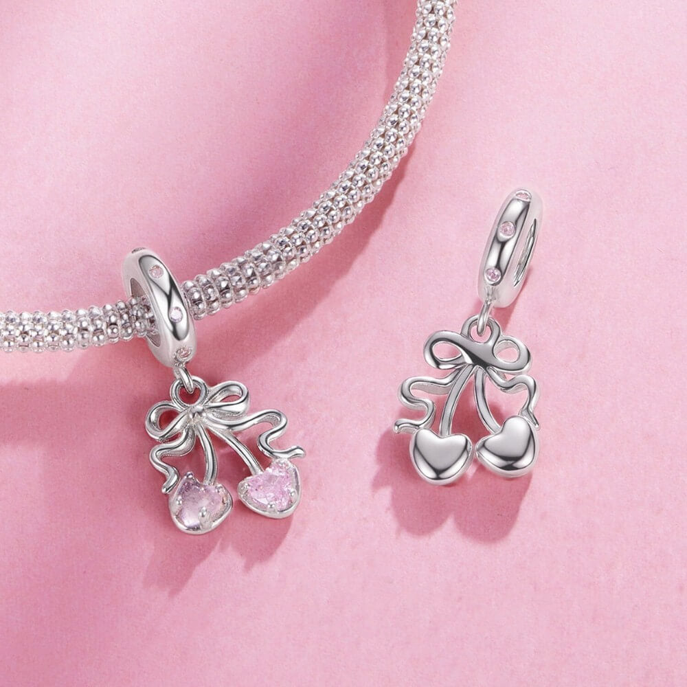 Sterling silver cherry charm with pink heart gemstones and bow detail.